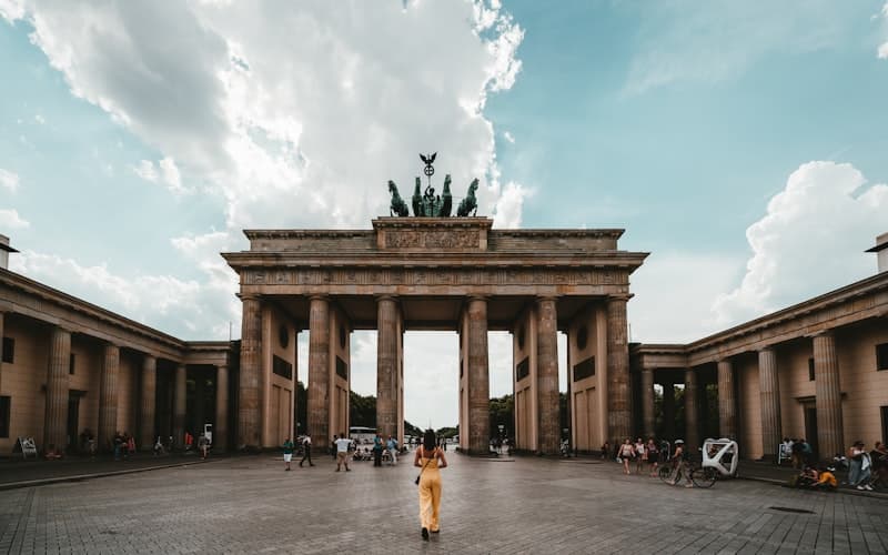 Person in Gelb geht über den Platz vor dem Brandenburger Tor unter Wolkenhimmel.