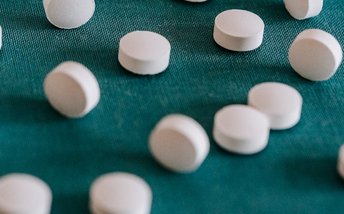 Round white tablets scattered across a dark teal cloth in soft light.