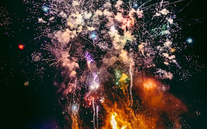 Kleurrijk vuurwerk met witte en oranje ontploffingen in een pikdonkere nachthemel.