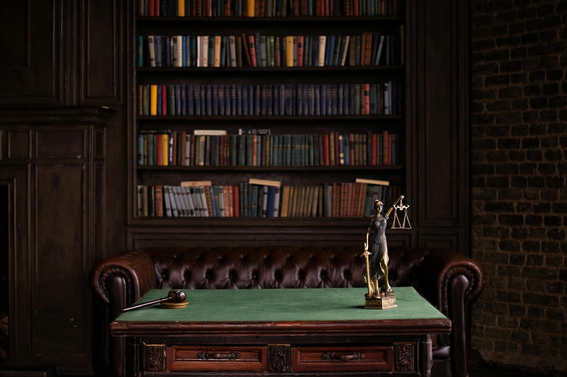 Justitia-Figur und Richterhammer auf einem grünen Tisch vor einem Bücherregal.