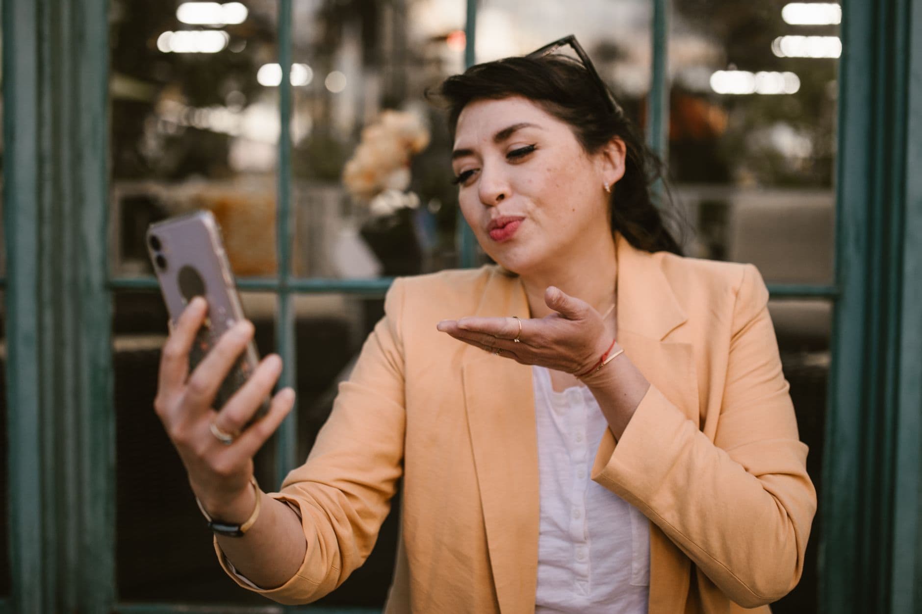 Une femme en blazer clair envoie un baiser à son téléphone pendant un appel vidéo.