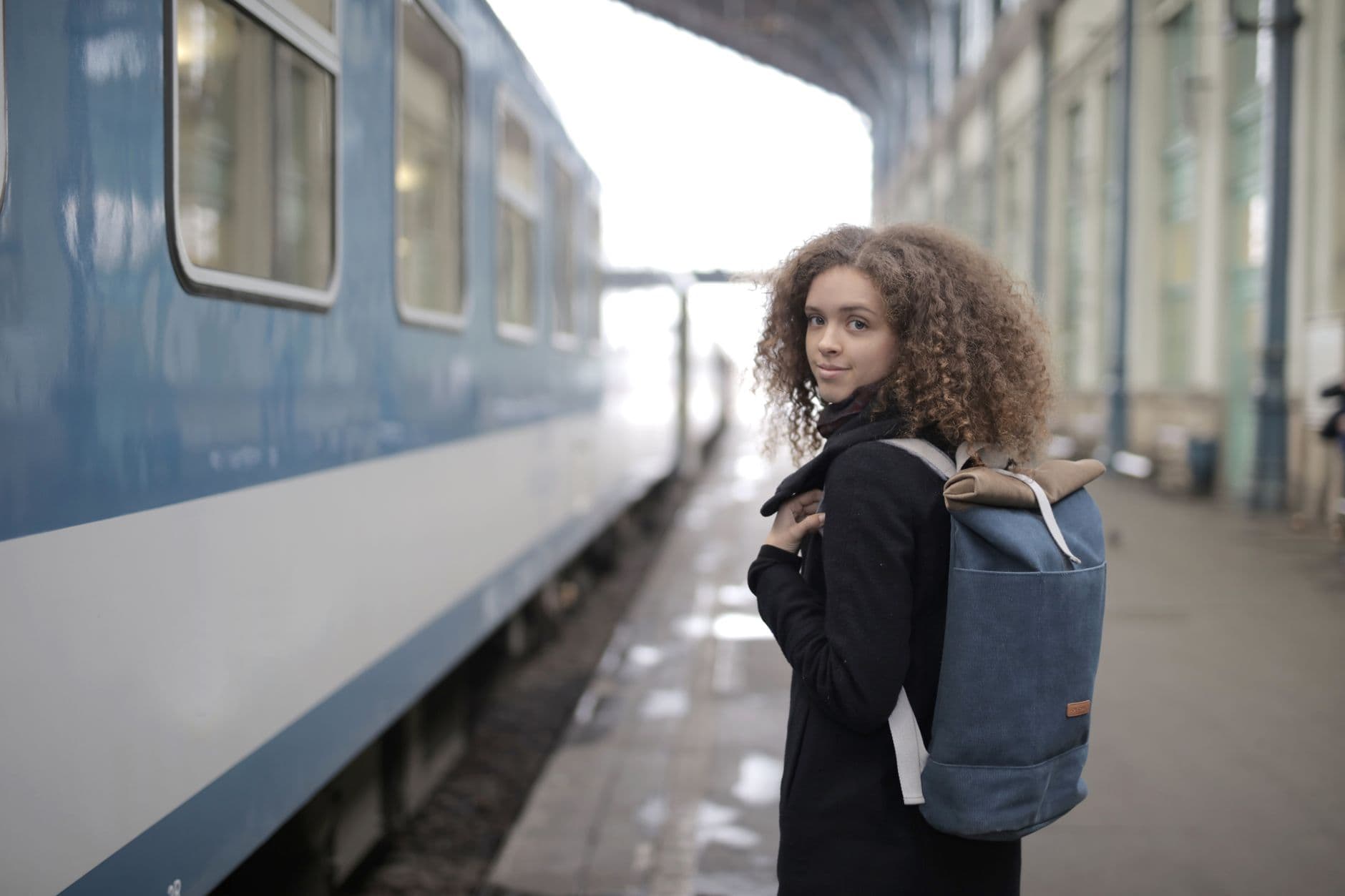 Una donna con lo zaino attende sul binario accanto a un treno.
