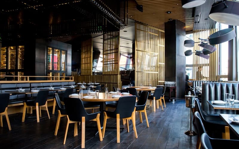 Leeg restaurant met gedekte houten tafels, donkere stoelen en hanglampen.