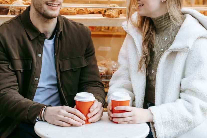 A smiling couple sharing a relaxed coffee date at a café, holding warm drinks