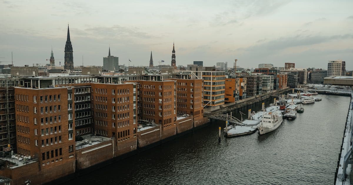 Backsteinhäuser und Boote am Hafenkanal unter grauem Himmel mit Kirchtürmen.