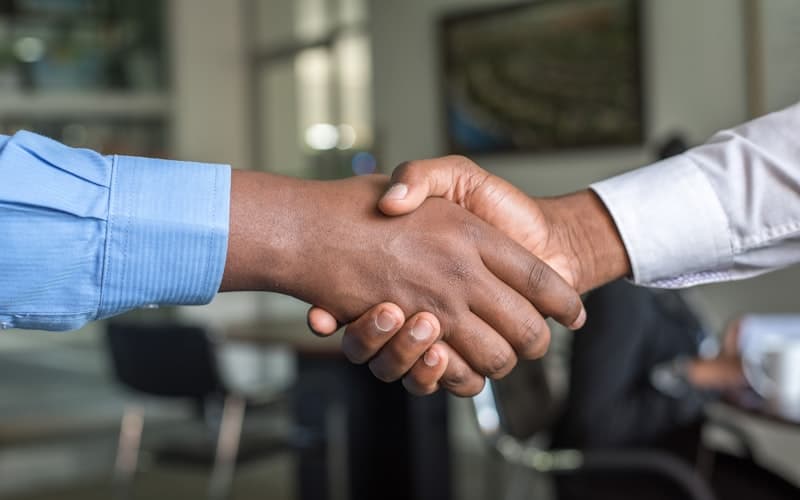 Zwei Personen geben sich in einem Büro die Hand, hellblaues und weißes Hemd.