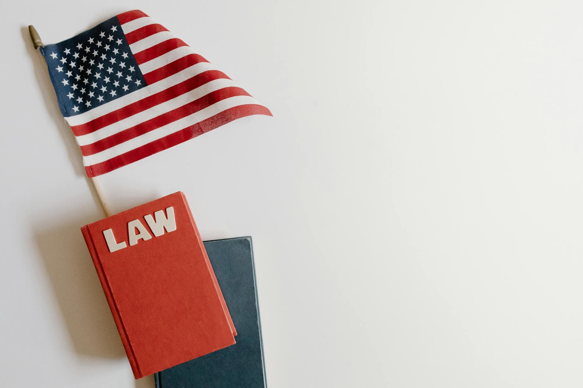 A small flag with stars and stripes leans over a red book marked LAW on a white surface.