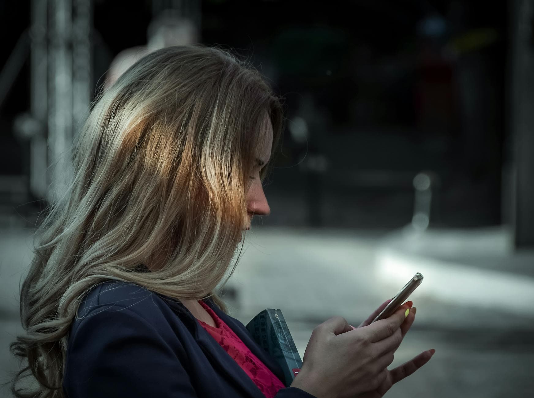 Person mit langen blonden Haaren im dunklen Blazer schaut auf ihr Smartphone.