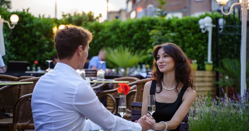 Well-dressed couple holding hands across the table over champagne on a restaurant terrace in the evening