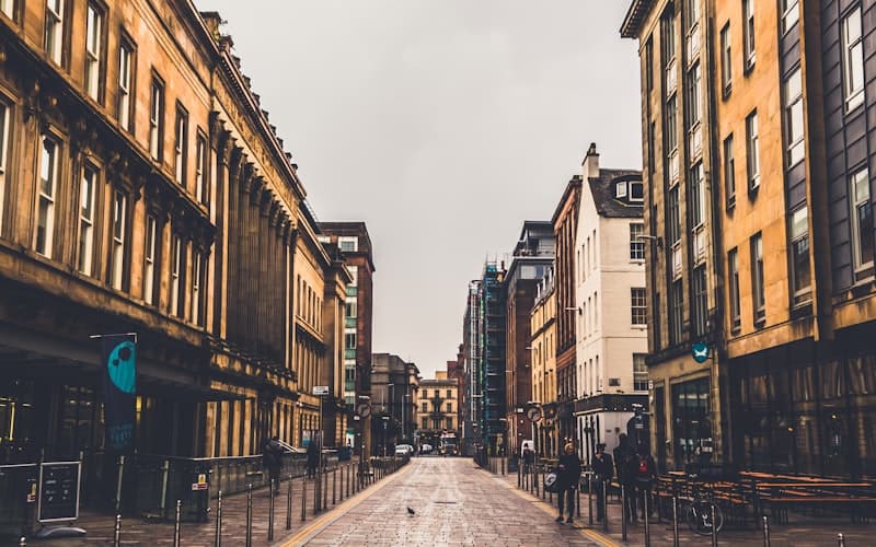 Lege winkelstraat met hoge stenen gebouwen en een paar wandelaars onder grijze lucht.