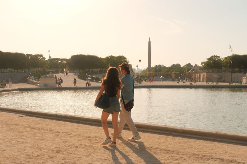 Een jong stel wandelt op een zomerse avond langs de grote fontein van de Tuilerieën in Parijs, met de obelisk van de Place de la Concorde op de achtergrond