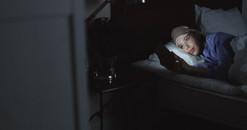 Woman lying in bed at night reading messages on her phone, her face lit by the screen