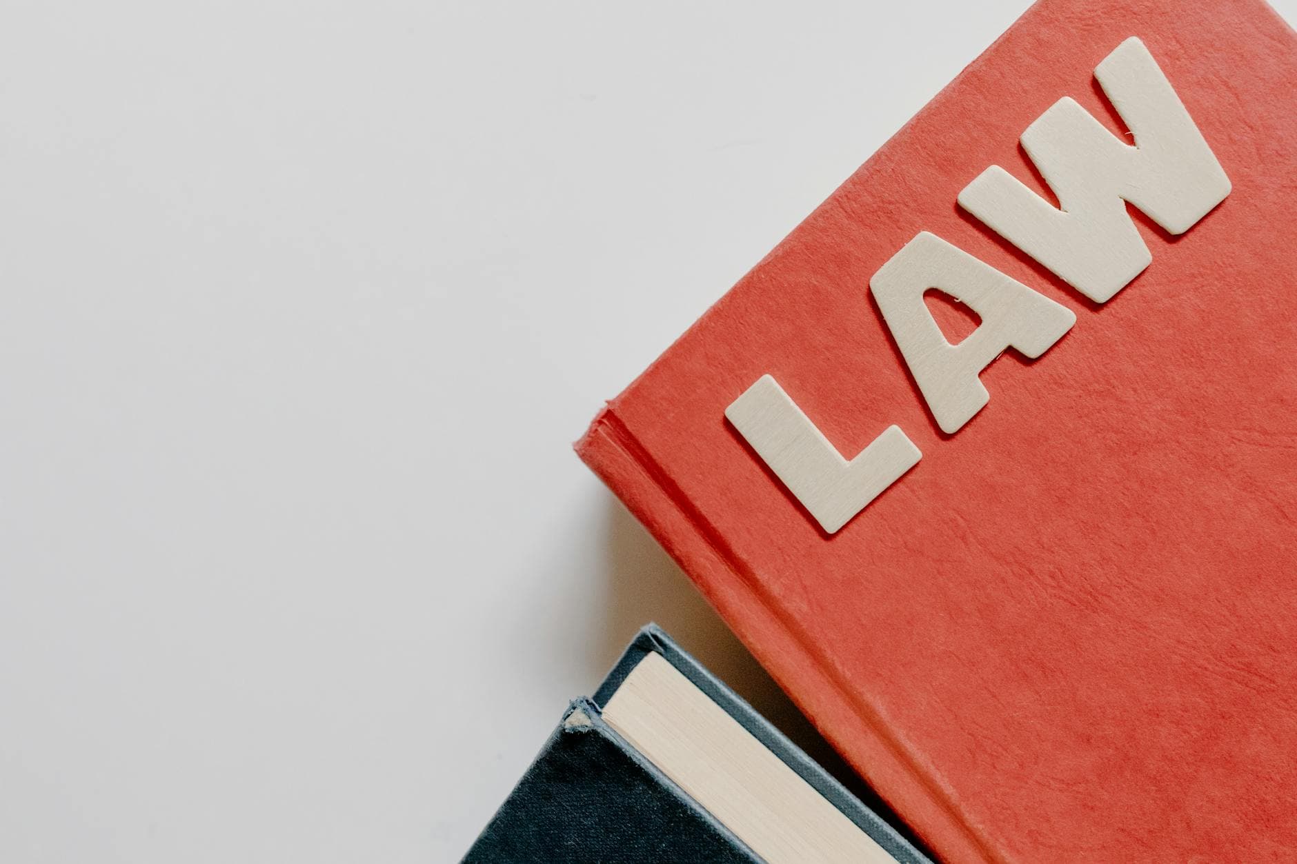 Röd bok med bokstäverna LAW i trä ovanpå en mörkblå bok mot vit bakgrund.