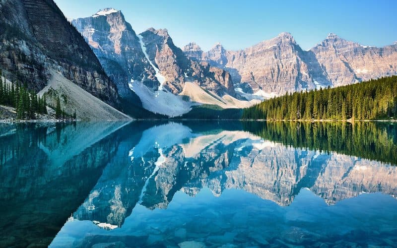Snow-capped peaks and pine forest mirrored in a still turquoise mountain lake.