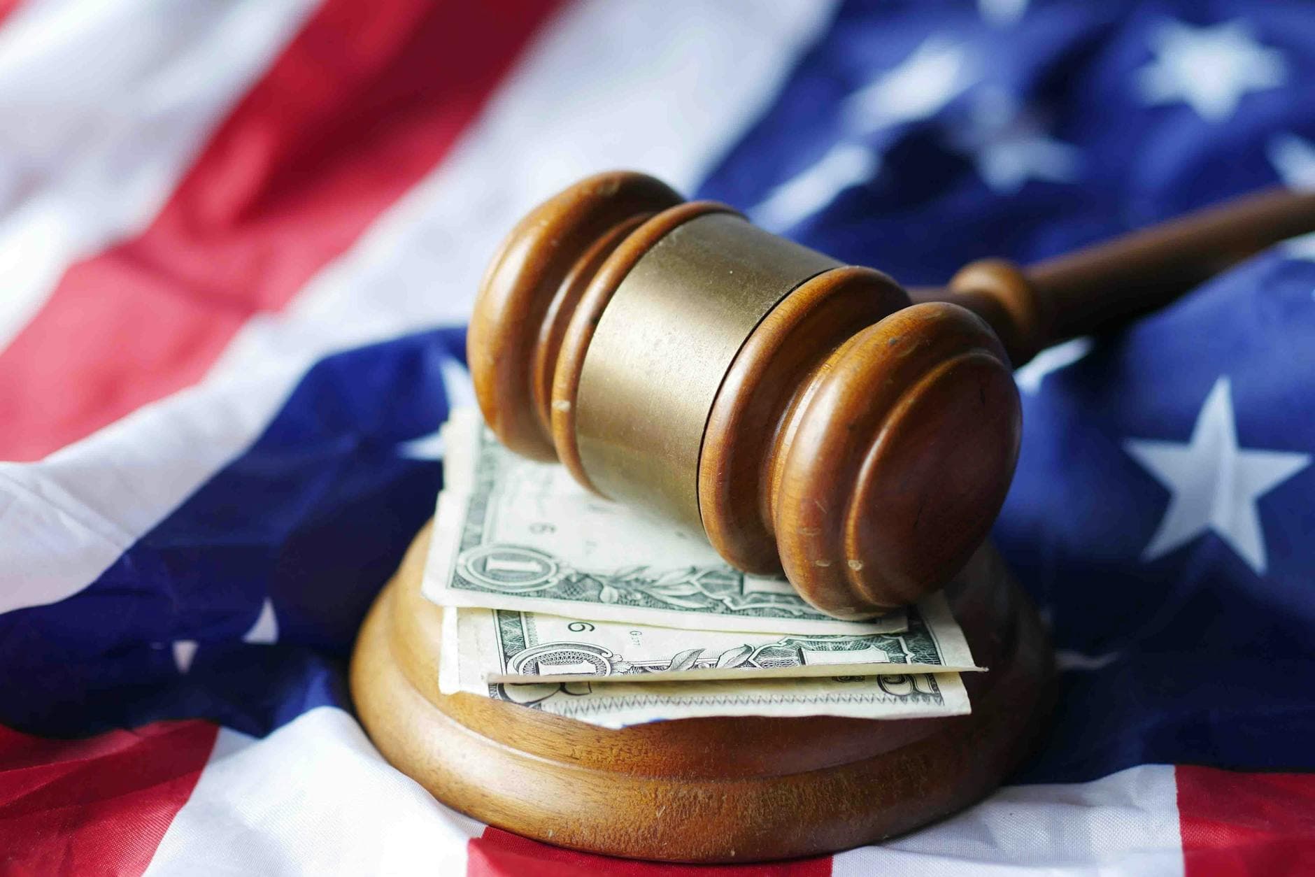 A wooden gavel rests on folded dollar bills laid over an American flag.