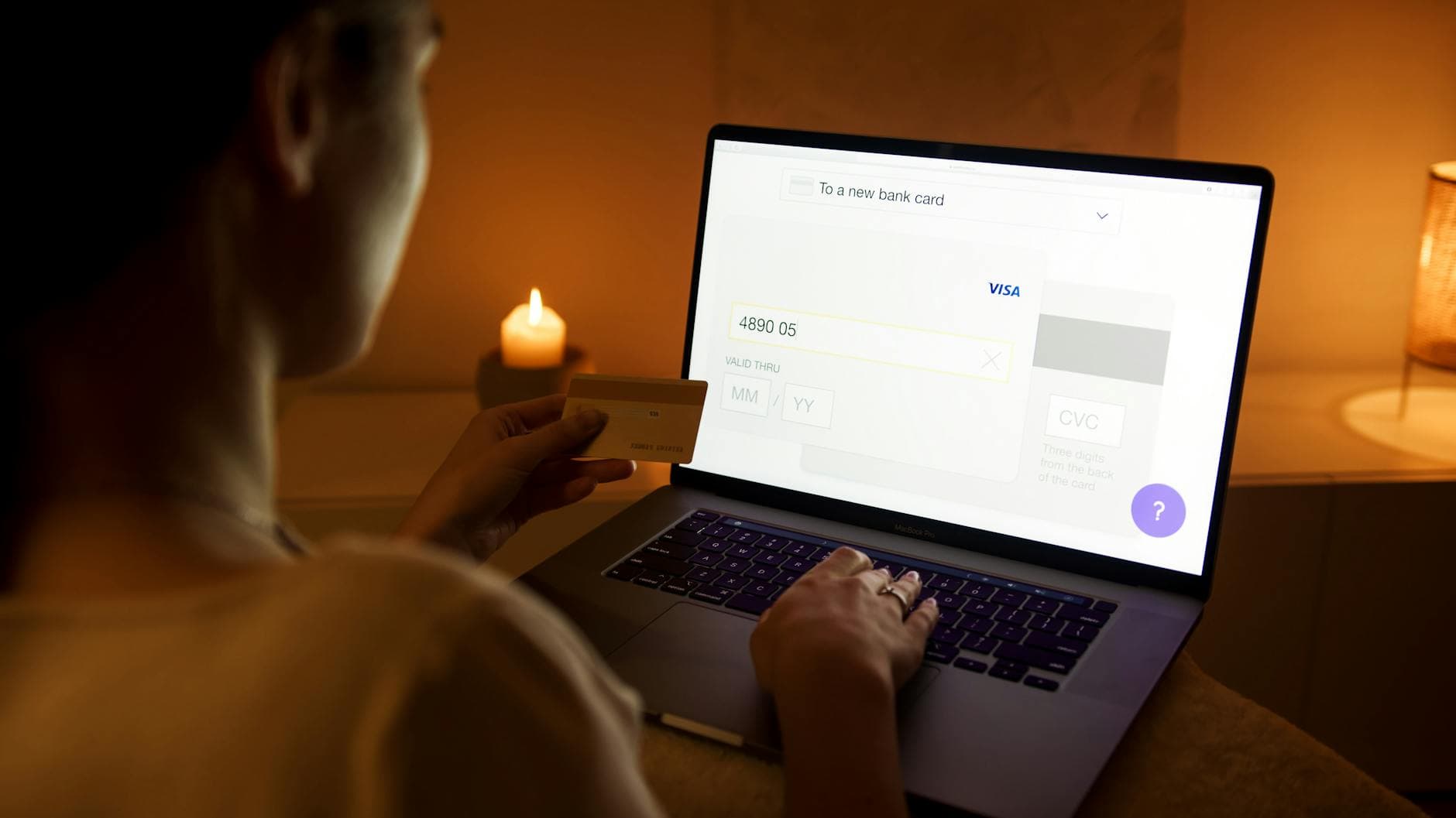 Iemand typt bij kaarslicht een bankpasnummer over op een laptop met een gouden pas in de hand.