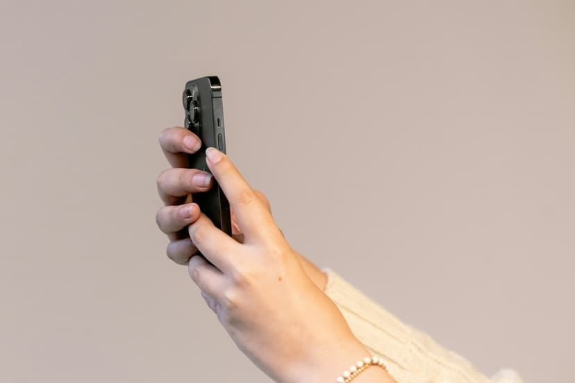 Handen van een vrouw in een crèmekleurige kabeltrui houden een smartphone omhoog voor een effen, lichte muur