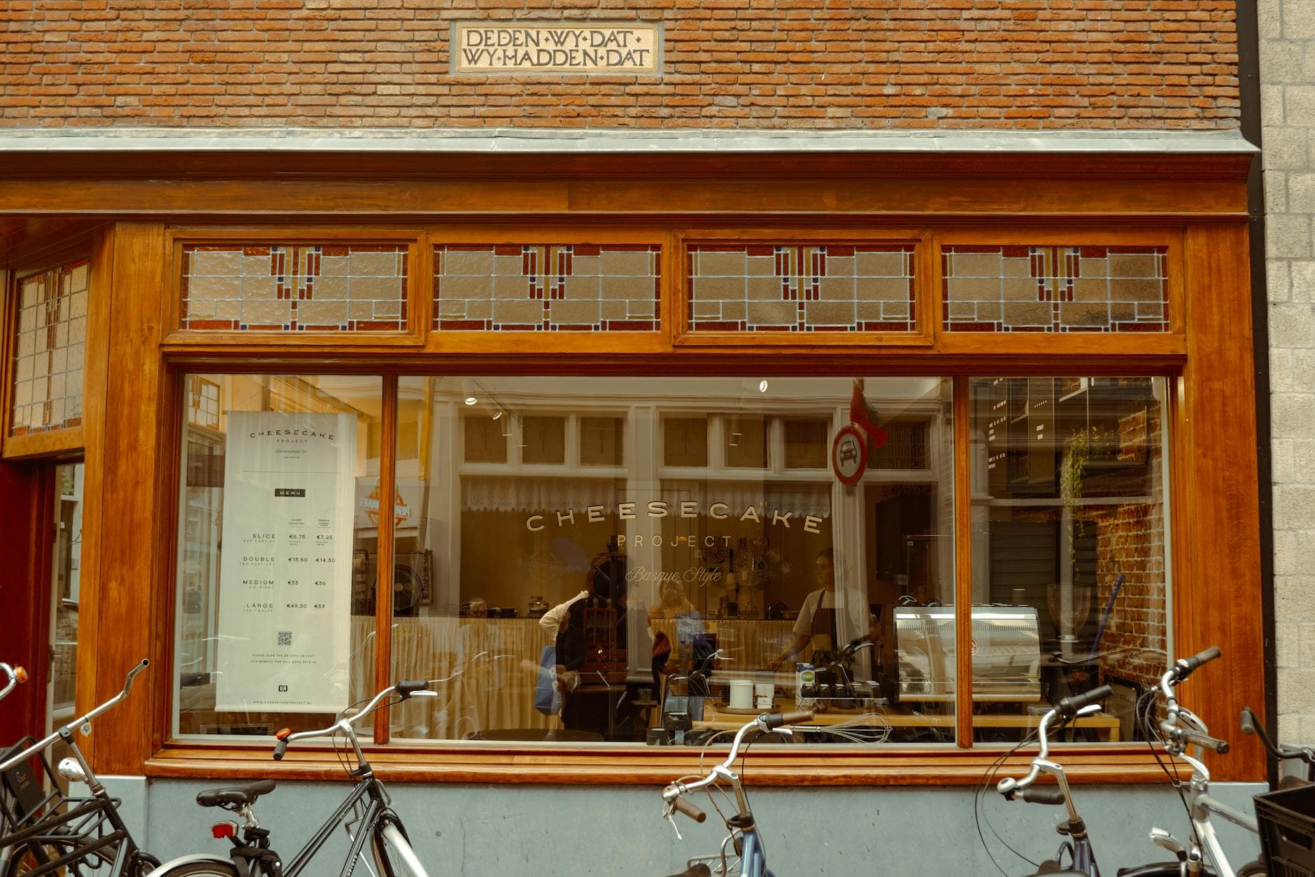 Houten winkelpui met glas in lood en geparkeerde fietsen voor een bakstenen gevel.
