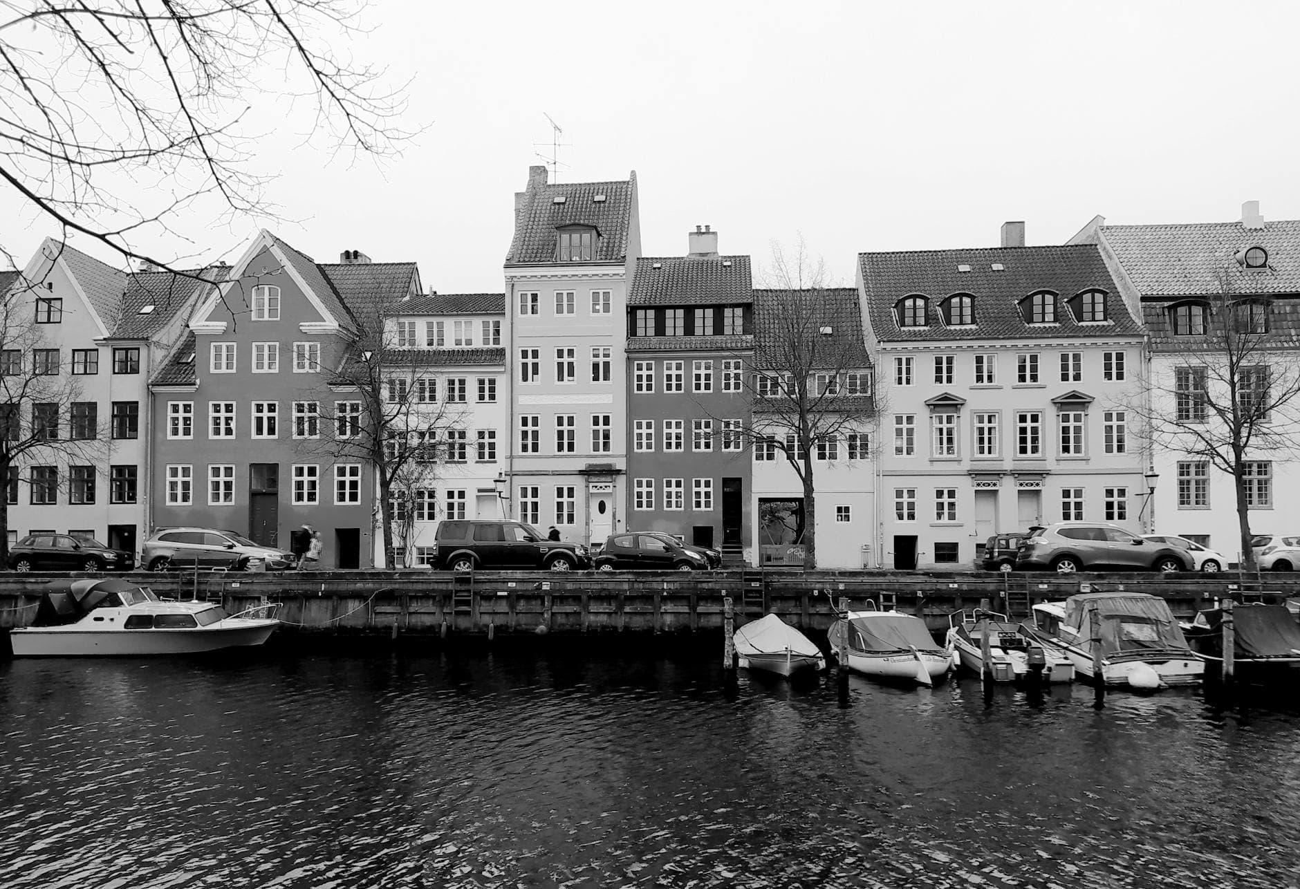 Sorthvidt motiv af gamle byhuse og små både langs en stille kanal.