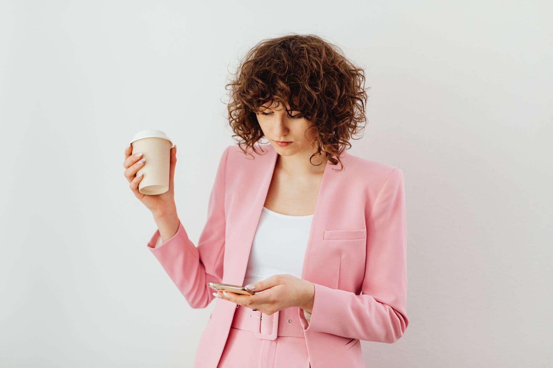 Una donna in un completo rosa tiene una tazza e guarda il telefono.