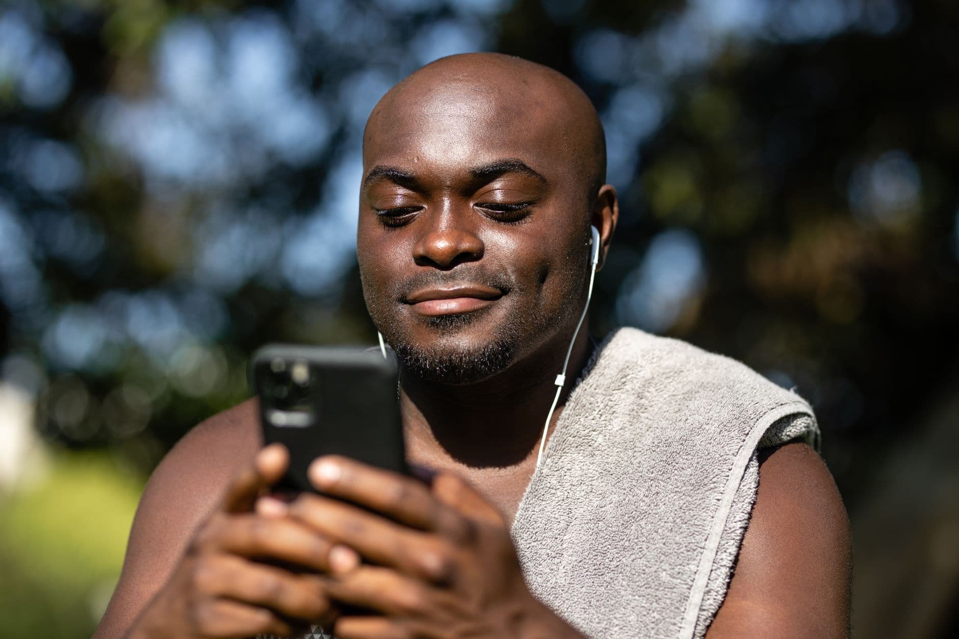 Мужчина с полотенцем на плече смотрит на смартфон на улице.