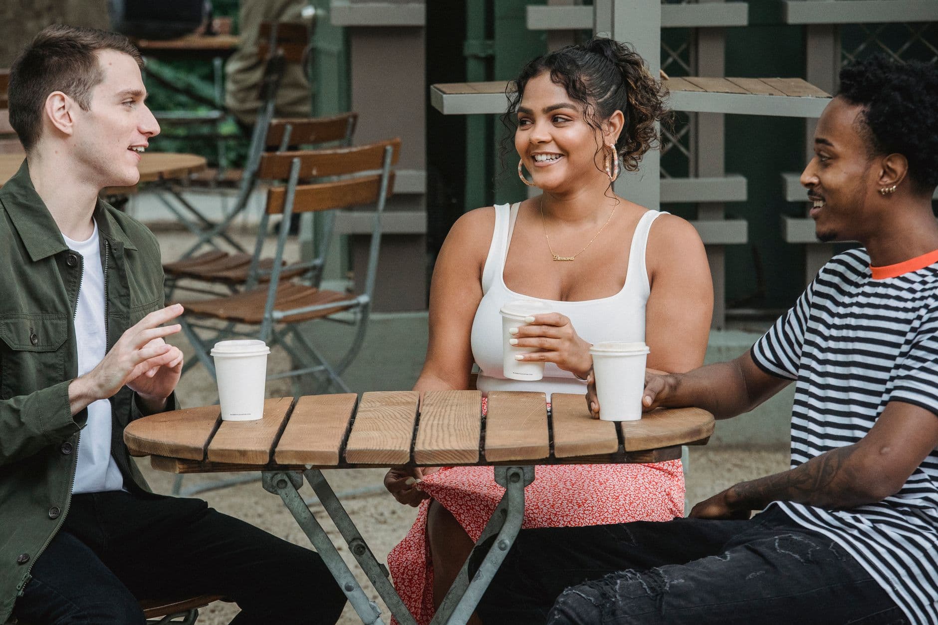 Drie volwassenen praten buiten een café met meeneembekers in de hand.