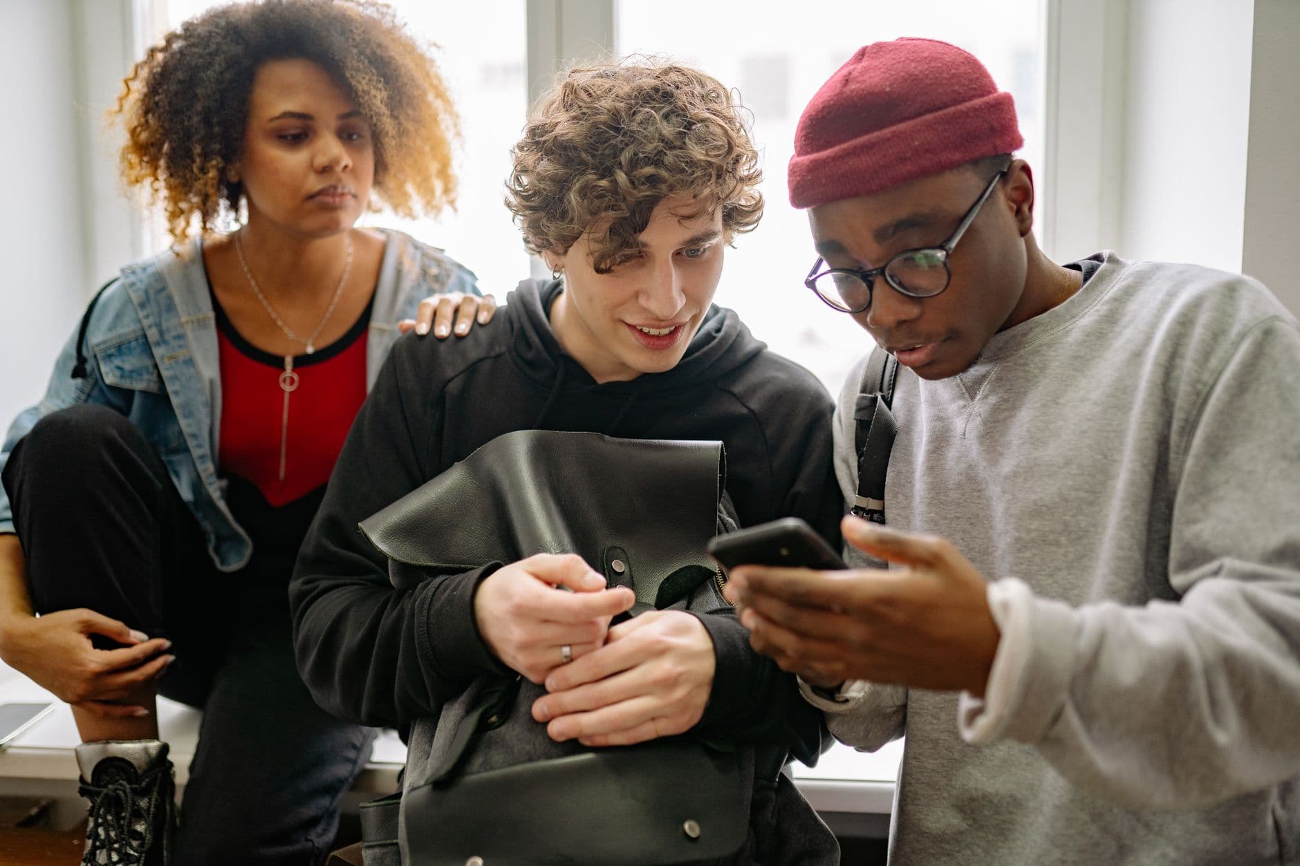 Drei junge Erwachsene schauen gemeinsam auf ein Smartphone, das einer von ihnen in der Hand hält.
