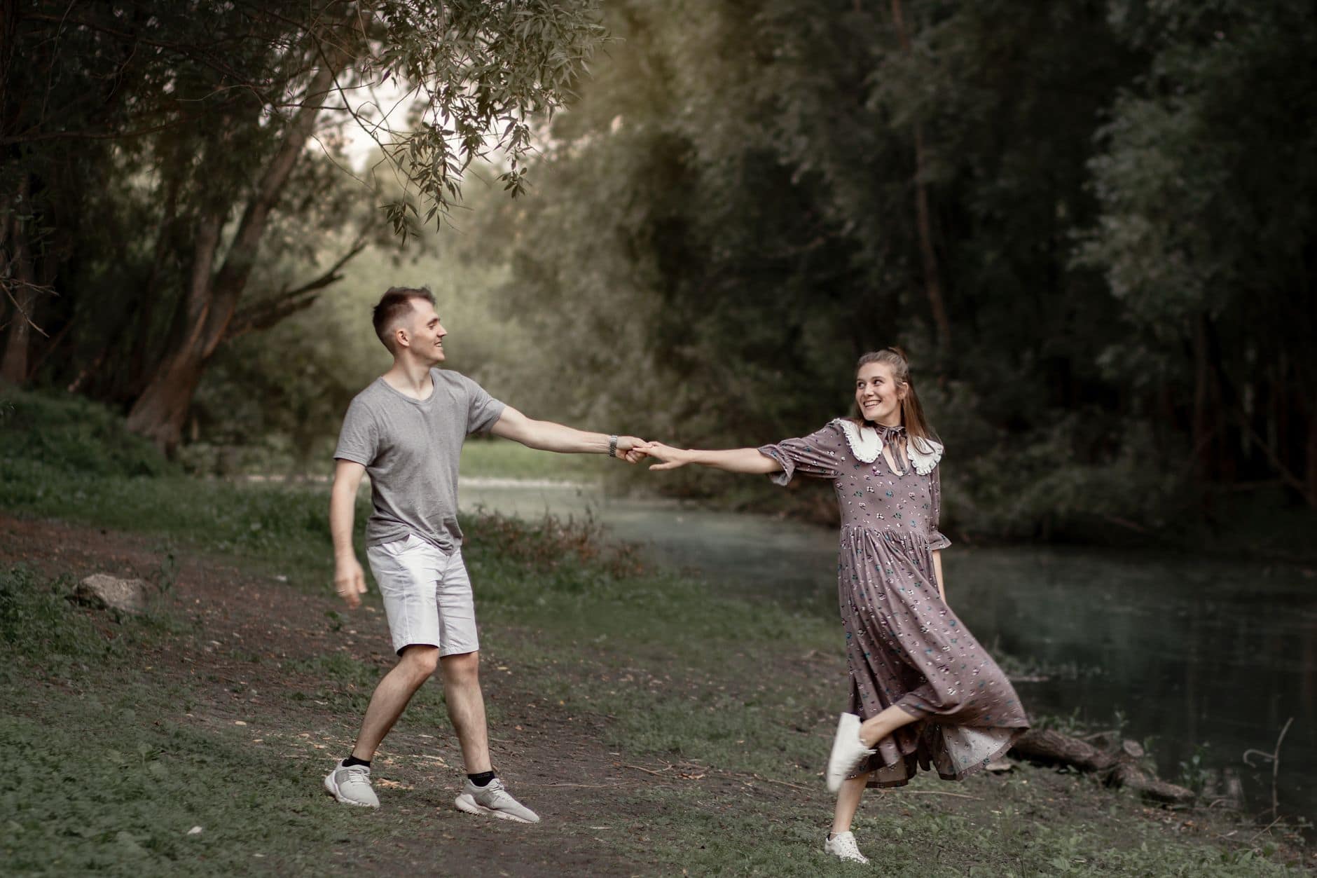 Een man en een vrouw houden elkaars hand vast en lachen op een pad tussen de bomen.