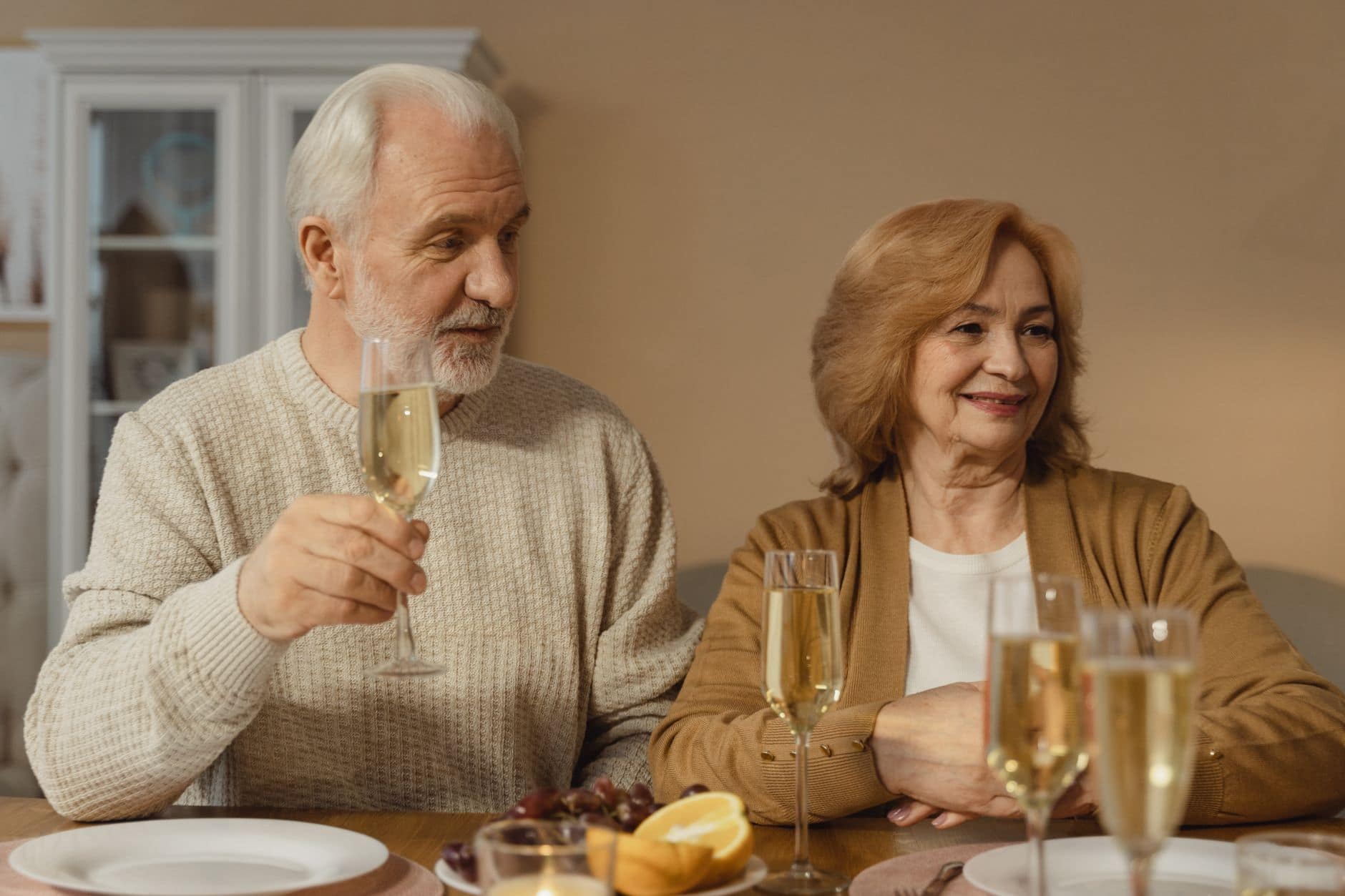 Dos personas adultas comparten un brindis en una mesa del comedor.