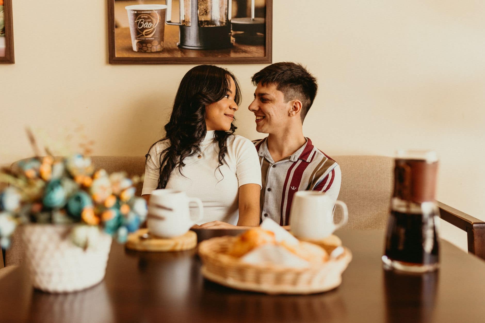 Een man en een vrouw zitten dicht bij elkaar en glimlachen aan een tafel met koffiekoppen.