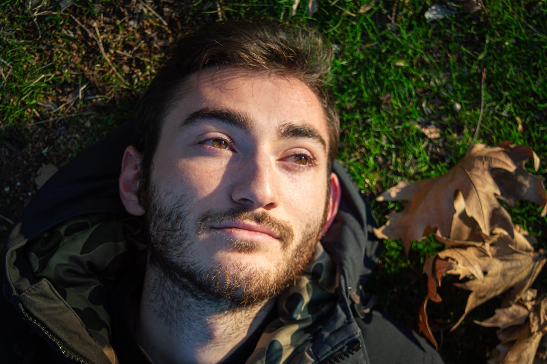 Portret mężczyzny z krótkim zarostem, leżącego na trawie w popołudniowym świetle